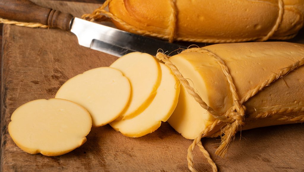 Provolone sir u valjku i narezan na okrugle kriške na drvenoj dasci