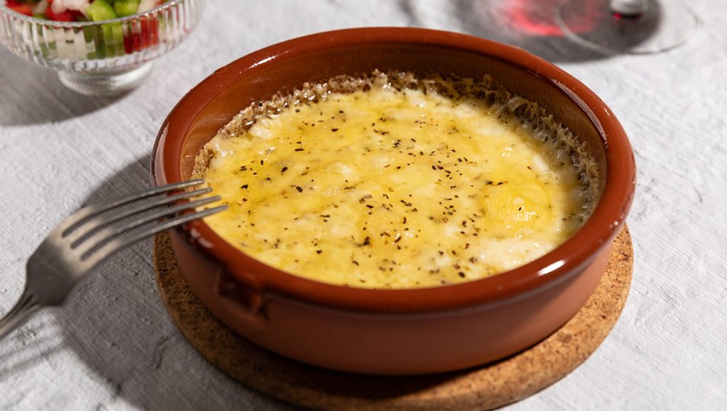 Provolone zapečen u keramičkoj posudi sa origanom, uz salatu i čašu vina